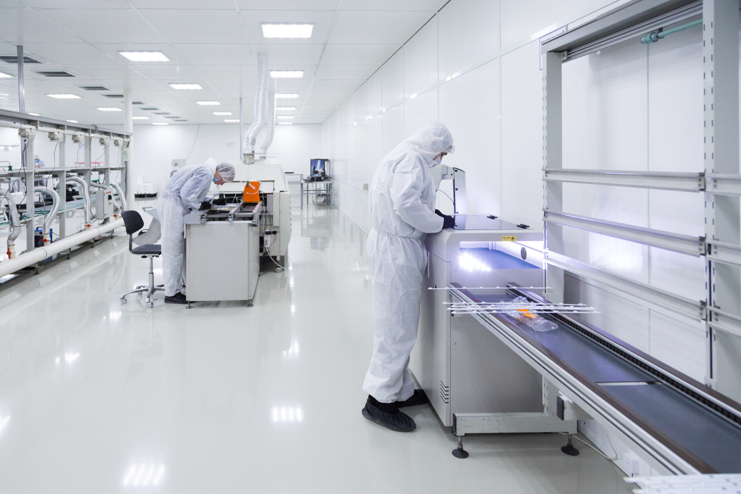 factory workers in white lab suits and black latex gloves, working with some modern equipment in a very clean room.